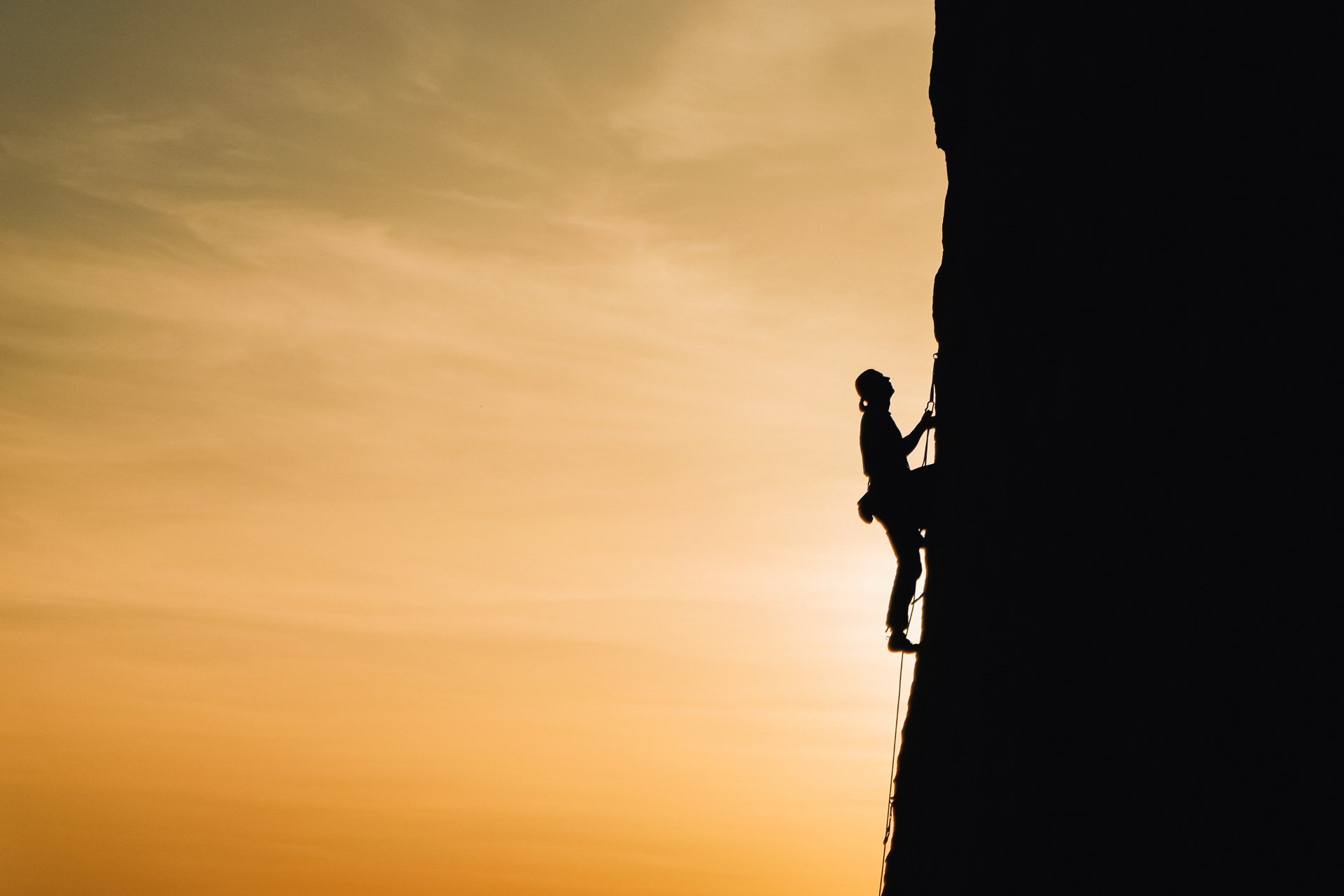 Una silueta de una persona escalando una pared de roca al atardecer.