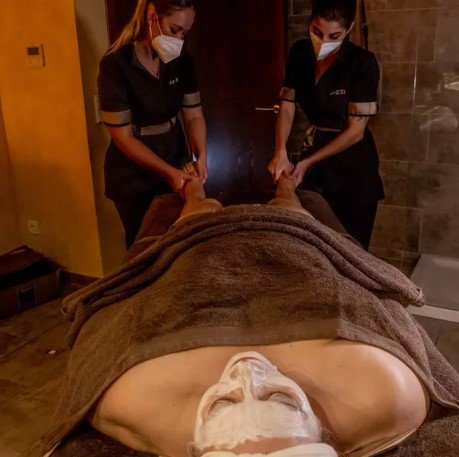 Dos mujeres con máscaras le están dando un masaje a un hombre en un spa.