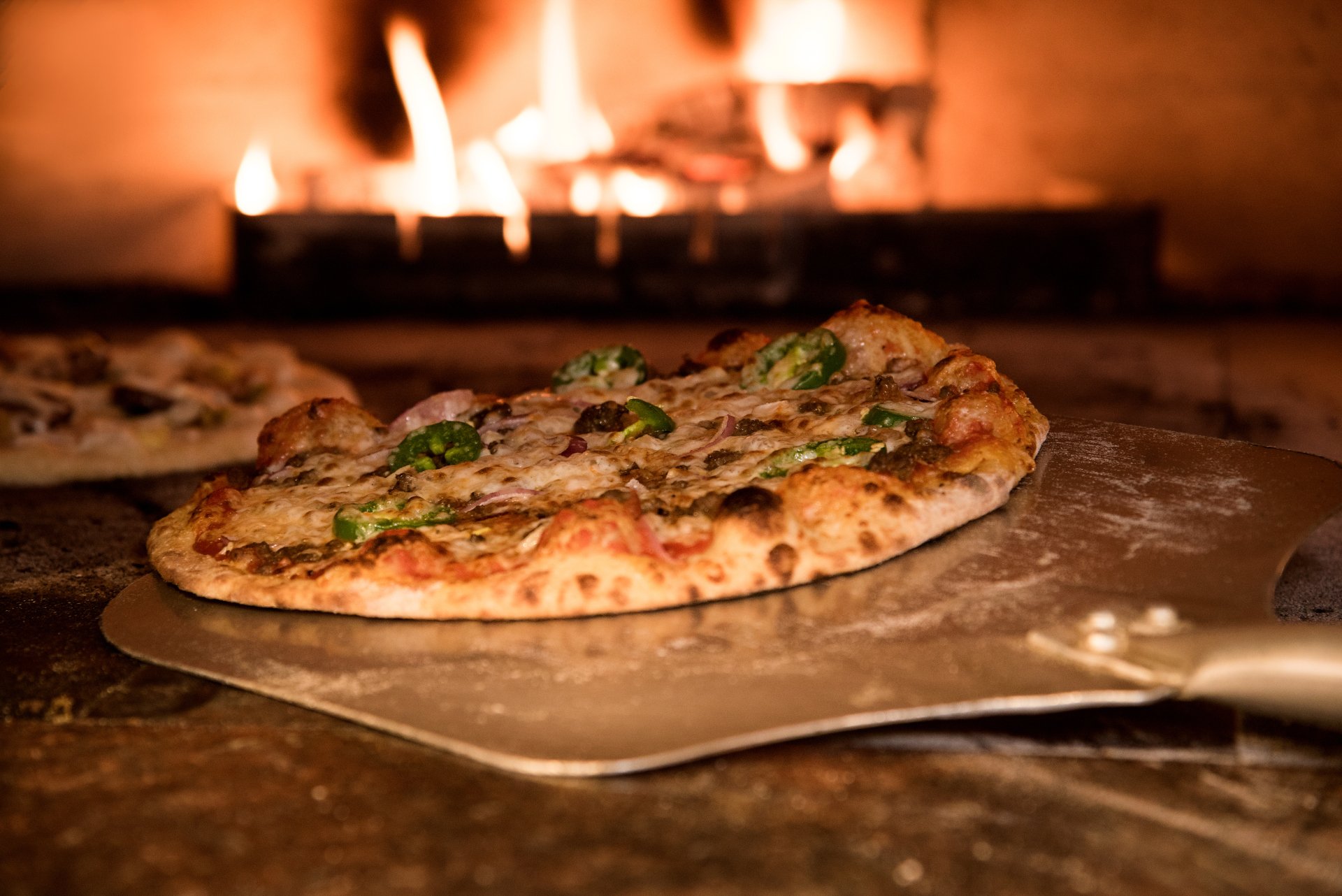 Una pizza reposa sobre una pala delante de una chimenea.