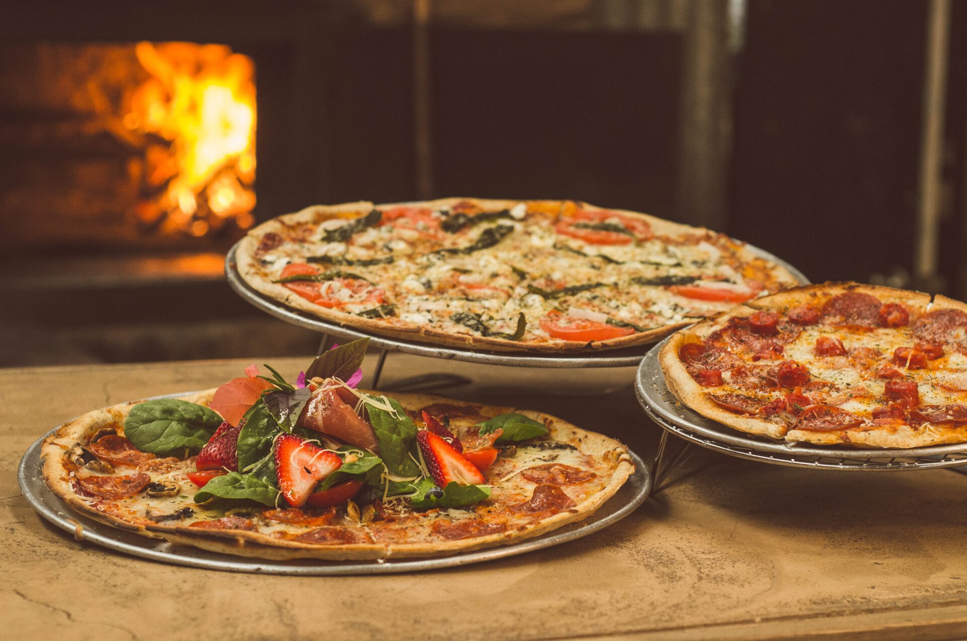 Tres pizzas están apiladas una encima de otra sobre una mesa de madera.