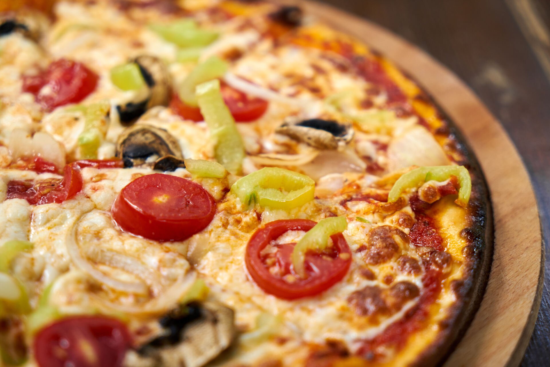 Una pizza con tomates, pimientos, champiñones y queso sobre una tabla de cortar de madera.